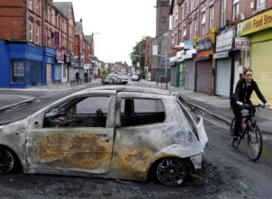A woman cycles past a burnt out car on Lawrence road in Wavertree, Liverpool, after a second night of rioting.