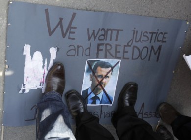 Protesters stand on a crossed picture of Syrian President Bashar Assad during a rally against his regime in front of the Syrian embassy in Belgrade.