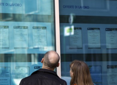 A couple checks jobs offers on the window of an employment agency in Milan.