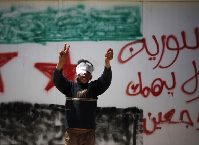 Syrian refugee Bashar al-Zalfi, 10, waves the victory sign while posing in front of a wall with the colors of the revolutionary flag, and Arabic reading,